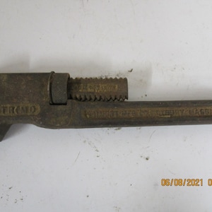 May include: A rusty pipe wrench with the text "TRIMO" and "MANUFACTURED BY TRIMO MASS." on the handle.