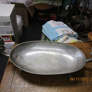 May include: A silver oval serving dish with two candle holders attached to the sides. The dish is on a wooden surface.