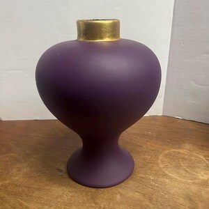 May include: A matte purple vase with a bulbous body and a flared base. The top of the vase has a gold-colored rim. The vase is a decorative item.