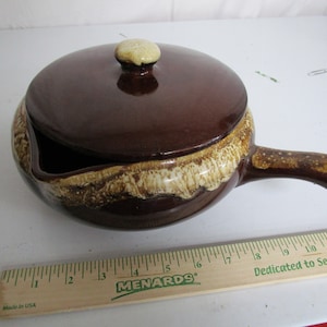 Puede incluir: Una cacerola de cerámica marrón con tapa y asa. La cacerola tiene un esmalte blanco y marrón con un patrón moteado. La cacerola tiene un diámetro de aproximadamente 18 cm.