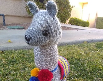May include: A crocheted gray llama with a colorful saddle and pom-poms. The llama is standing on green grass. *Pattern Only*