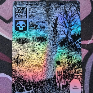 May include: Holographic art print featuring a surreal landscape with a figure standing near a body of water. The image includes Japanese text and a skull emblem. The words "Yo. Tambien..." are in a speech bubble.