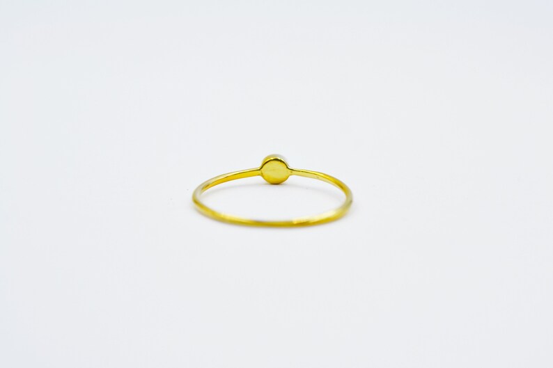 以下が含まれることがあります： 中央に丸いオパールがセットされたシンプルなゴールドリングです。