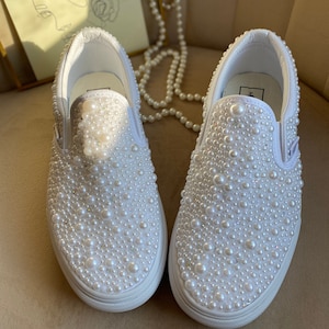 Puede incluir: Zapatillas blancas de lona sin cordones cubiertas de perlas blancas.