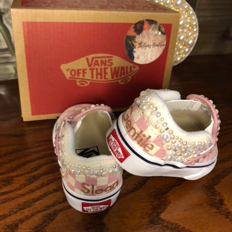 Puede incluir: Un par de zapatos Vans a cuadros rosa y blanco con adornos de perlas. Los zapatos est&aacute;n personalizados con los nombres "Sloan" y "Sentile".
