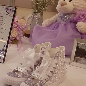 May include: A pair of white high-top sneakers with a purple and white design. The sneakers are covered in rhinestones and have the words "Mis 15 A&ntilde;os" written on them.