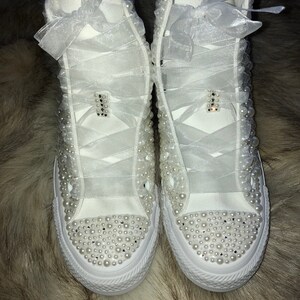 May include: White high-top sneakers with pearl embellishments and white satin ribbon laces.