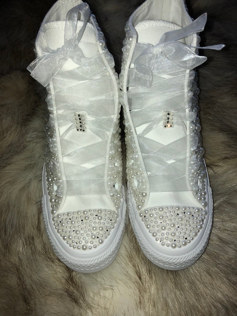 May include: White high-top sneakers with pearl embellishments and white satin ribbon laces.