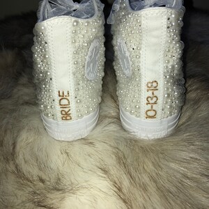 May include: White high-top sneakers with pearl embellishments. The left shoe says "BRIDE" and the right shoe says "10-13-18".