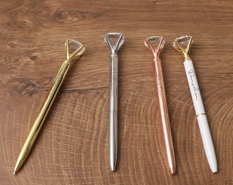 May include: Four pens with diamond-shaped tops in gold, silver, rose gold, and white. The white pen has the word "Darling" written on it.