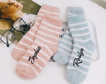 Puede incluir: Dos pares de calcetines rayados de felpa con los nombres "Sophia" y "Roslyn" bordados. Los calcetines son rosa y azul.