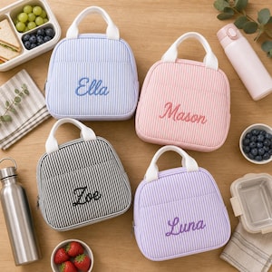 Puede incluir: Cuatro bolsas t&eacute;rmicas para el almuerzo con asas blancas y patrones de rayas en azul claro, rosa, negro y morado. Cada bolsa tiene un nombre bordado en la parte frontal: Ella, Mason, Zoe y Luna. Las bolsas est&aacute;n dispuestas con recipientes y botellas.