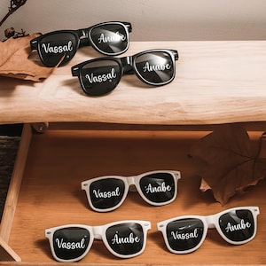 May include: Six pairs of sunglasses with black frames and lenses. The sunglasses have the names "Vassal" and "Anabe" printed on the lenses in white.