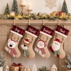 May include: Four tan burlap Christmas stockings hanging in a row, each featuring a red and black buffalo plaid cuff with a white embroidered name: Ivy, Oliver, Emma, and Theo. Each stocking displays a plush character: a polar bear, reindeer, snowman, and Santa Claus, all wearing scarves and accented with embroidered antlers and colourful string lights.