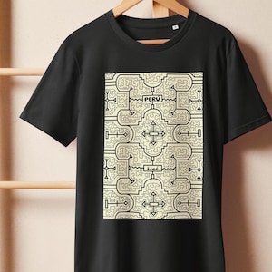 May include: Black t-shirt featuring a cream-colored geometric design with the word "PERU" and "kené" in black. The design is a repeating pattern of lines and shapes. The shirt is hanging on a wooden hanger.