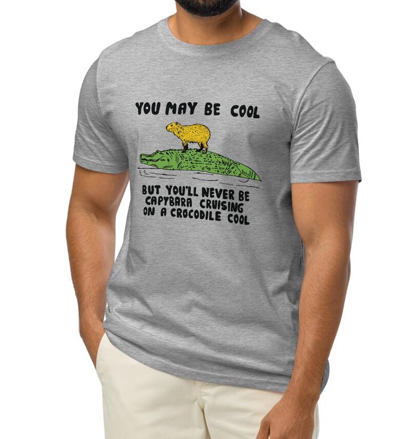 May include: A gray t-shirt with the text "You may be cool but you'll never be capybara cruising on a crocodile cool."  A cartoon image of a capybara riding a crocodile is above the text.