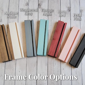 Op de afbeelding: Acht houten frames in verschillende kleuren, waaronder donker walnoot, antiek wit, verweerd grijs, vintage aqua, rode schuur, roze bloemblaadjes en klassiek zwart. De frames zijn allemaal even groot en van dezelfde vorm, en ze zijn in een rij van links naar rechts gerangschikt. De tekst "Frame Kleuropties" staat onder de frames.