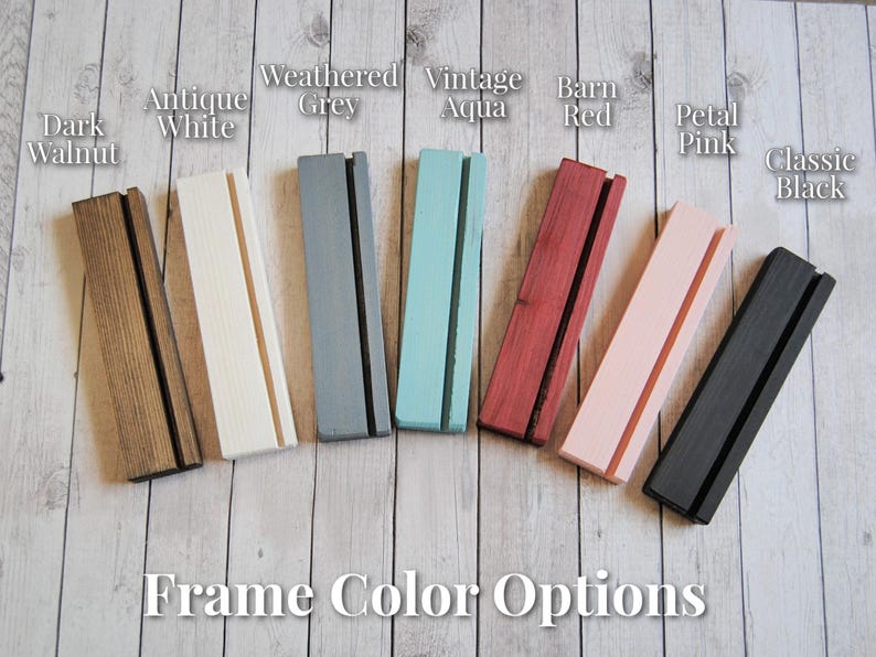Op de afbeelding: Acht houten frames in verschillende kleuren, waaronder donker walnoot, antiek wit, verweerd grijs, vintage aqua, rode schuur, roze bloemblaadjes en klassiek zwart. De frames zijn allemaal even groot en van dezelfde vorm, en ze zijn in een rij van links naar rechts gerangschikt. De tekst "Frame Kleuropties" staat onder de frames.