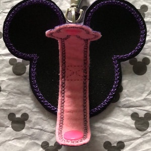 May include: A pink and black Mickey Mouse-shaped key chain with a purple trim and a silver clip.