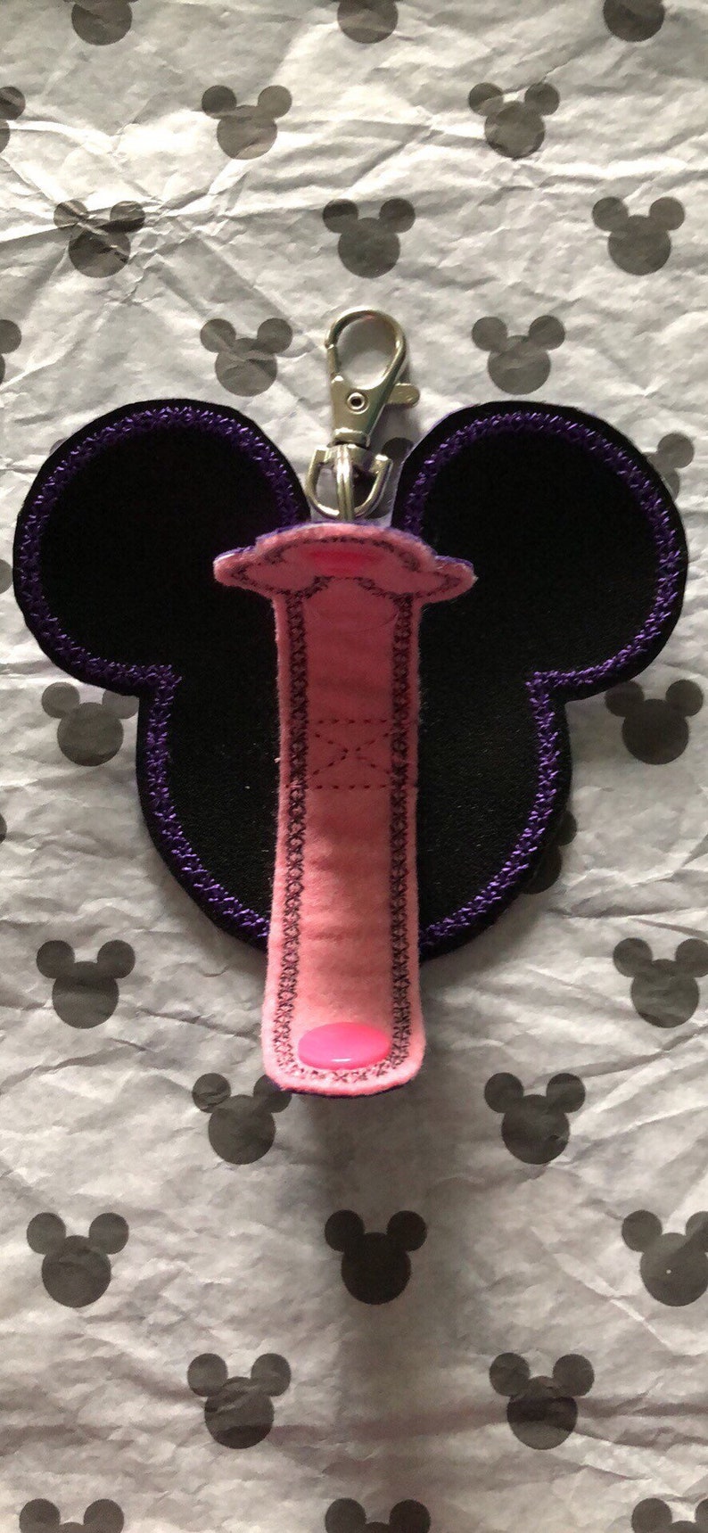 May include: A pink and black Mickey Mouse-shaped key chain with a purple trim and a silver clip.