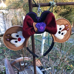May include: Chipmunk character ears headband with a burgundy bow and a black and purple key chain holder.