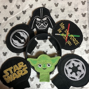 Peut inclure: Un ensemble de six bandeaux d'oreille en feutre noir sur le thème de Star Wars. Les bandeaux présentent des images brodées de Dark Vador, Yoda, le symbole de l'Alliance rebelle, le symbole impérial et les mots "Star Wars" et "Que la Force soit avec toi".