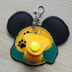 May include: A yellow and green Mickey Mouse-shaped key chain with a paw print design. The key chain has a yellow button and a silver metal clasp.