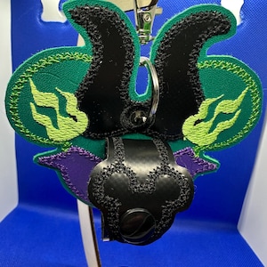 May include: A green, black and purple embroidered key chain with a black leather loop and a silver metal ring. The key chain features a stylised design of a creature with flames.