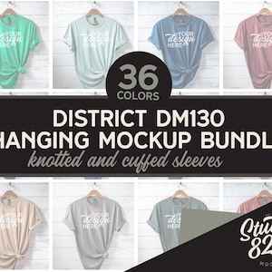 Puede incluir: Un paquete de maquetas de 36 camisetas de diferentes colores colgadas en perchas con mangas anudadas y dobladas. Las camisetas son todas del mismo estilo y tienen el texto "YOUR DESIGN HERE" impreso en ellas. El texto "DISTRICT DM130 HANGING MOCKUP BUNDLE knotted and cuffed sleeves" está impreso en la parte inferior de la imagen. El texto "36 COLORS" está impreso en el centro de la imagen. El texto "Studio 825 MOCKUPS" está impreso en la esquina inferior derecha de la imagen.