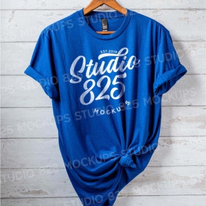 May include: A royal blue t-shirt with a white graphic design that says "Studio 825" and "Est. 2019". The shirt is hanging on a wooden hanger against a white wood background.