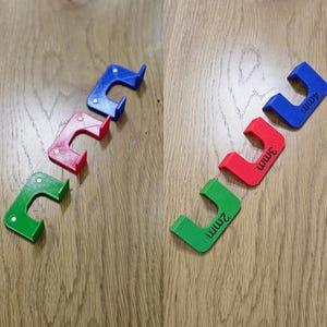 May include: Three brightly coloured, plastic, U-shaped tools in green, red, and blue, each with a small white dot. The tools are labelled with the measurements 2mm, 3mm, and 4mm. They are arranged on a wooden surface.
