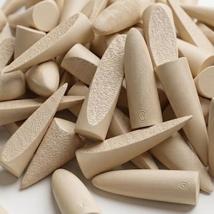 Puede incluir: Un conjunto de tacos de madera de color beige claro en varias formas, incluyendo cónicas, cilíndricas y en forma de cuña. Algunos tacos tienen superficies texturizadas con patrones de círculos concéntricos o pequeñas protuberancias. Los tacos están dispersos.