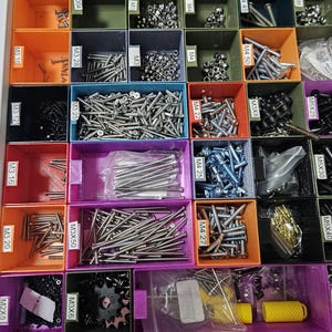 May include: A multi-compartment storage unit filled with various hardware items. The compartments, in shades of orange, green, purple, and blue, contain screws, bolts, and other small metal parts. Labels indicate sizes like M3, M4, and M5.
