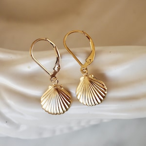 May include: A pair of gold-tone earrings featuring a seashell design. The earrings have a leverback closure.