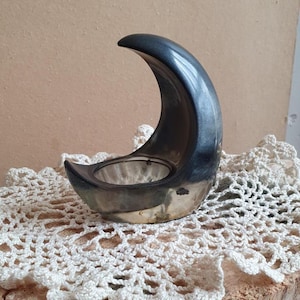 Peut inclure: Un bougeoir en forme de croissant de lune avec une finition lisse gris anthracite et argent métallique. L'objet présente un sommet incurvé et pointu ainsi qu'une ouverture centrale circulaire conçue pour accueillir une petite bougie.