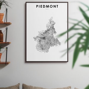 May include: A black and white map of Piedmont, Italy, in a black frame, hanging on a white wall. The map is a detailed illustration of the region's roads and cities.