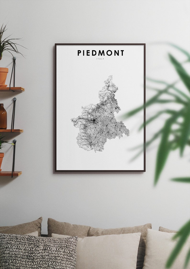 May include: A black and white map of Piedmont, Italy, in a black frame, hanging on a white wall. The map is a detailed illustration of the region's roads and cities.