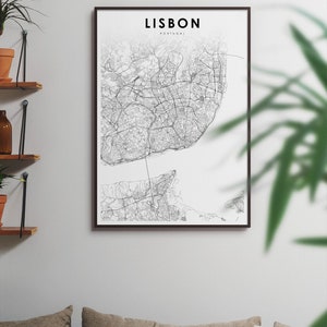 May include: A black and white map print of Lisbon, Portugal, in a black frame. The map shows the city's streets and waterways. The print is hanging on a white wall above a couch with brown cushions.