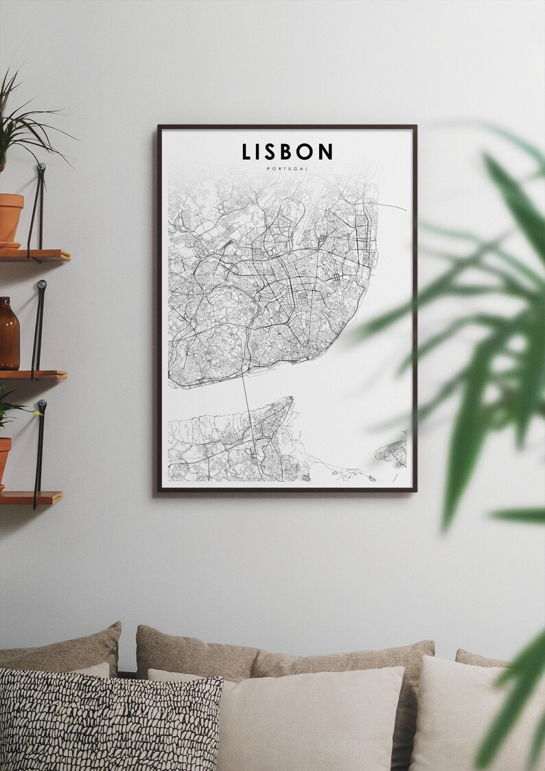 May include: A black and white map print of Lisbon, Portugal, in a black frame. The map shows the city's streets and waterways. The print is hanging on a white wall above a couch with brown cushions.