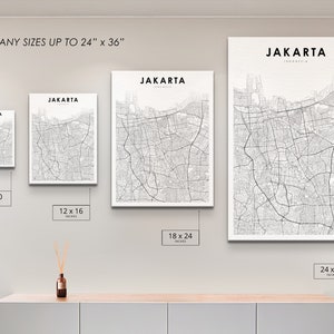 May include: Four different sizes of a black and white map print of Jakarta, Indonesia. The prints are displayed on a white wall with a wooden shelf underneath. The sizes are 8x10 inches, 12x16 inches, 18x24 inches, and 24x36 inches.