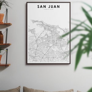 May include: A black and white map print of San Juan, Puerto Rico, in a brown frame. The map is displayed on a white wall above a couch with brown cushions.