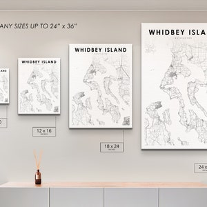 May include: Four different sizes of a black and white map print of Whidbey Island, Washington. The prints are displayed on a white wall with a light wood shelf underneath. The sizes are 8x10 inches, 12x16 inches, 18x24 inches, and 24x36 inches.