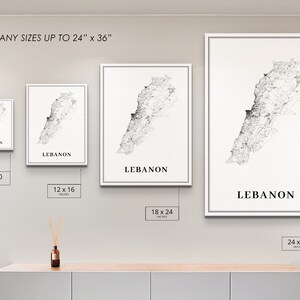 May include: Four framed prints of a black and white map of Lebanon, with the word "Lebanon" printed below each map. The prints are shown in different sizes: 8x10 inches, 12x16 inches, 18x24 inches, and 24x36 inches. The prints are displayed on a white wall with a wooden shelf below.