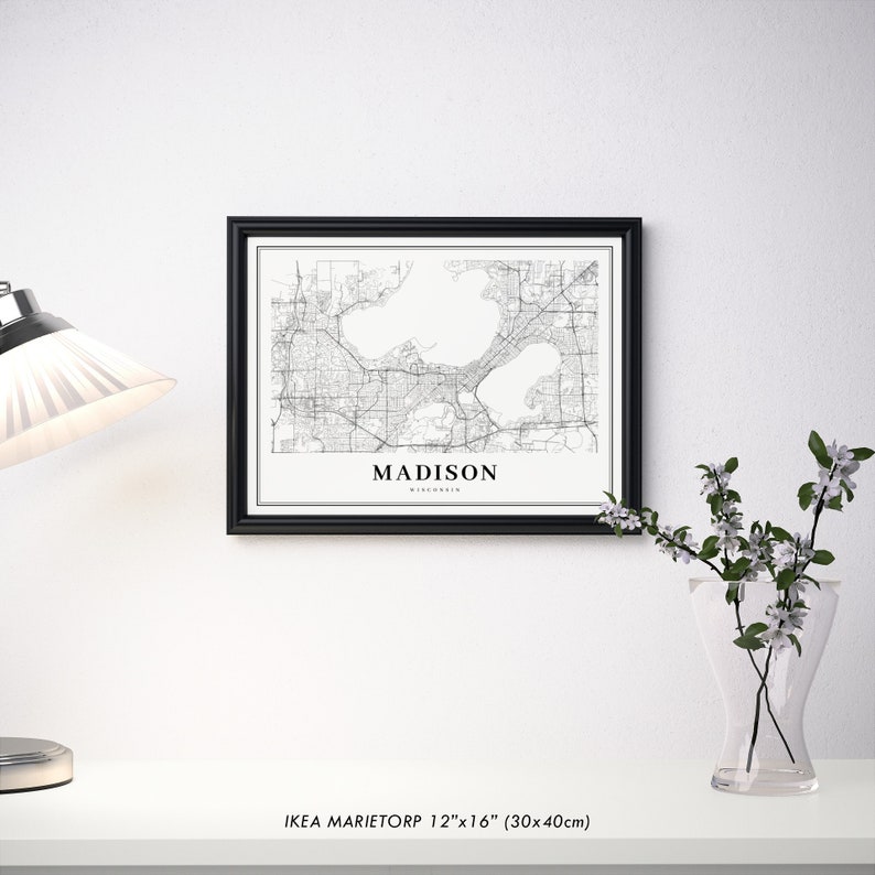 May include: Black and white map print of Madison, Wisconsin in a black frame. The map shows the city's streets and lakes. The print is 12 inches by 16 inches.