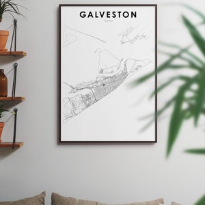 May include: A black and white line art map print of Galveston, Texas, in a black frame. The map is on a white background. The print is hanging on a white wall above a couch with pillows.