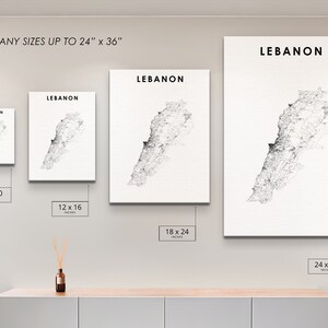 May include: A white wall with four framed prints of a black and white map of Lebanon. The prints are in different sizes: 8x10 inches, 12x16 inches, 18x24 inches, and 24x36 inches. The text "LEBANON" is printed at the top of each print. The prints are hanging on a white wall above a wooden shelf.
