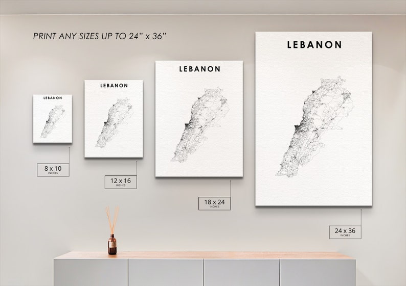 May include: A white wall with four framed prints of a black and white map of Lebanon. The prints are in different sizes: 8x10 inches, 12x16 inches, 18x24 inches, and 24x36 inches. The text "LEBANON" is printed at the top of each print. The prints are hanging on a white wall above a wooden shelf.