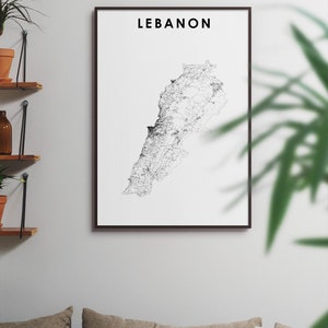 May include: A black and white line art print of the country of Lebanon in a black frame. The print is hanging on a white wall above a couch with pillows.