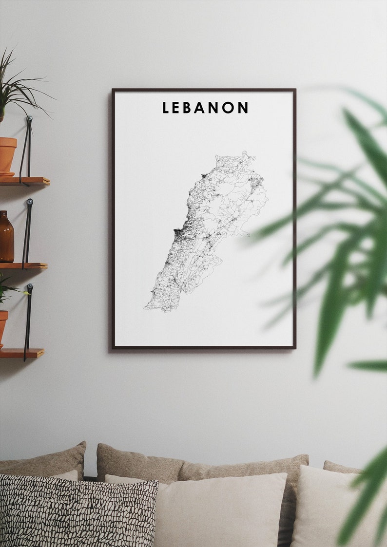 May include: A black and white line art print of the country of Lebanon in a black frame. The print is hanging on a white wall above a couch with pillows.
