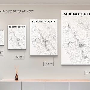 May include: A white wall with four framed maps of Sonoma County, California, in different sizes. The maps are printed in black and white and show the roads and towns of the county. The frames are all white and have a simple design. The text "PRINT ANY SIZES UP TO 24" x 36"" is printed at the top of the wall. The sizes of the maps are 8 x 10 inches, 12 x 16 inches, 18 x 24 inches, and 24 x 36 inches.